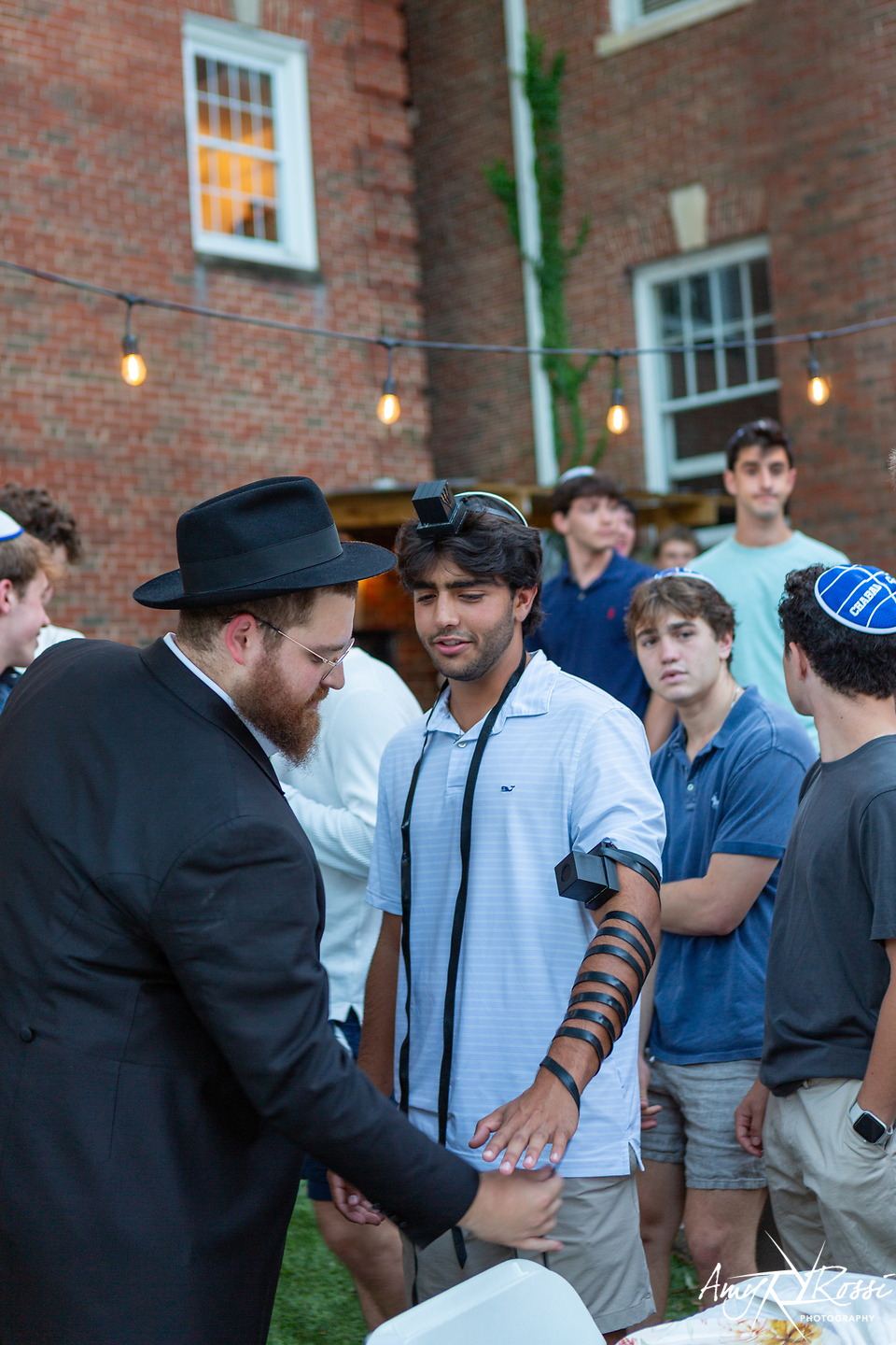 Rabbi Nossen helping a student wrap tefillin on the porch