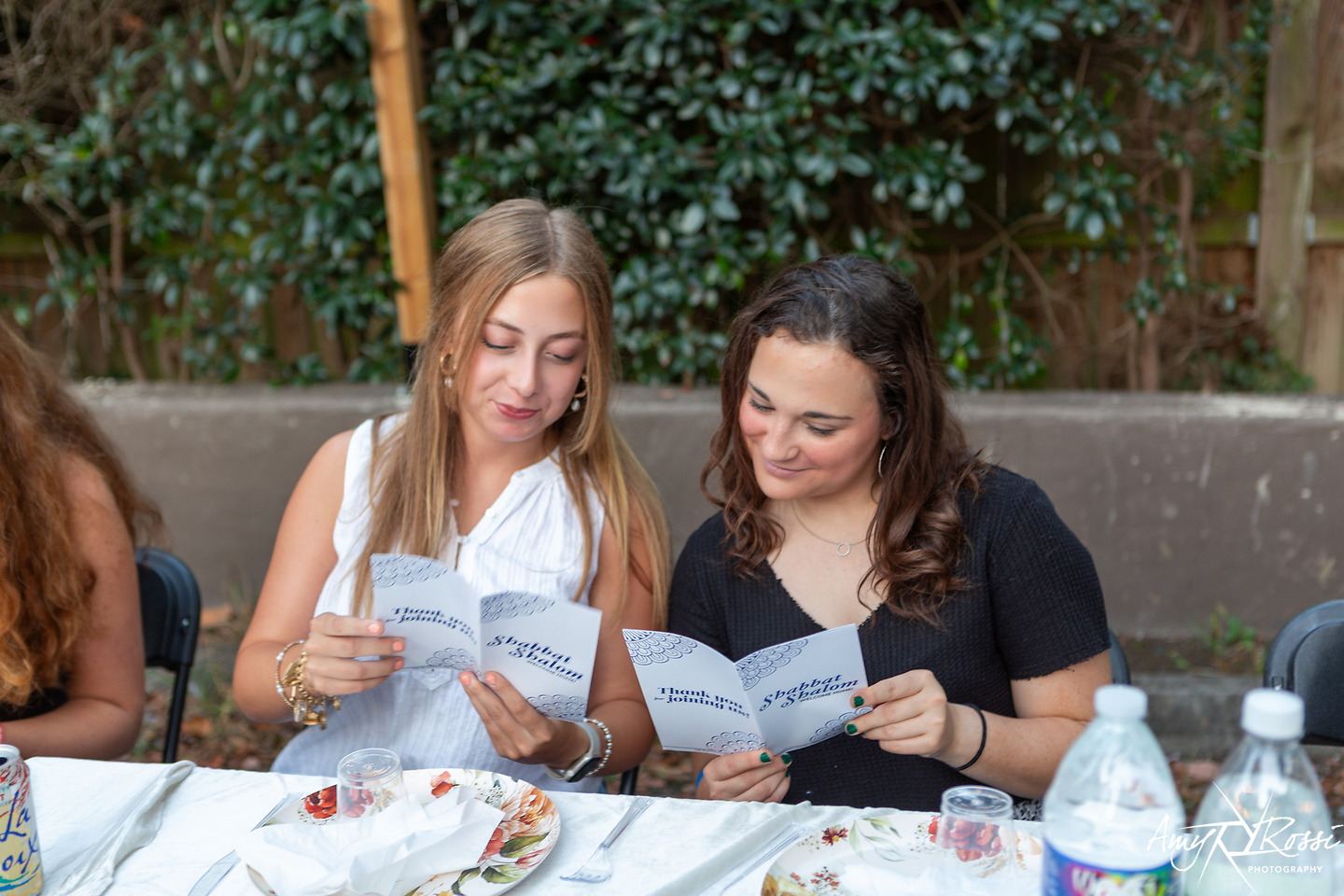 Two students reading benchers together at the Shabbat table
