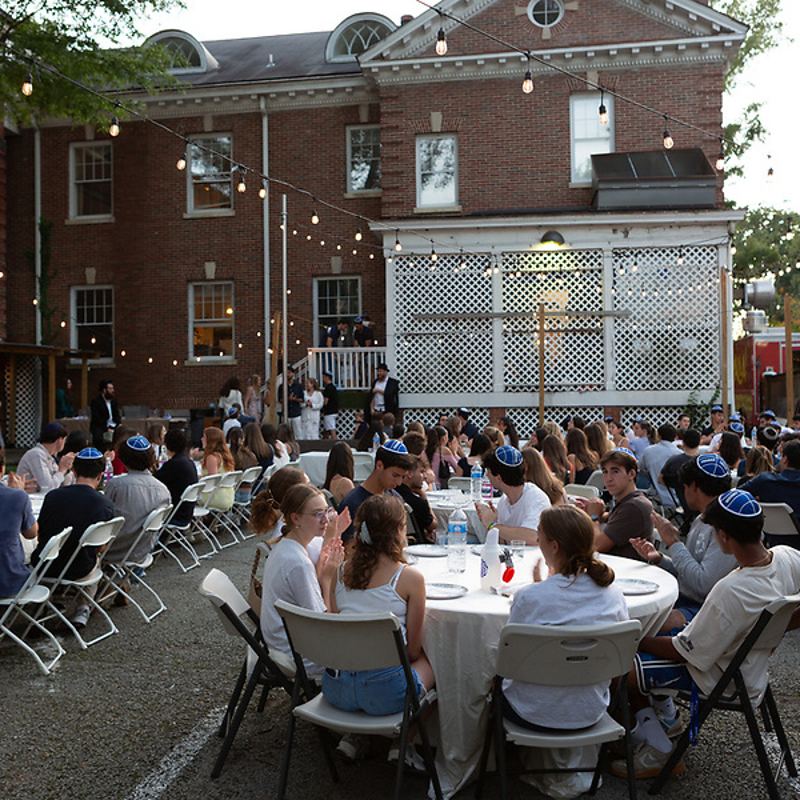 Students at round tables in front of the Fleishman House