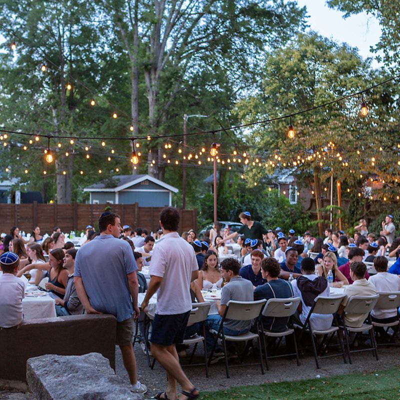 A packed Shabbat dinner crowd under the trees