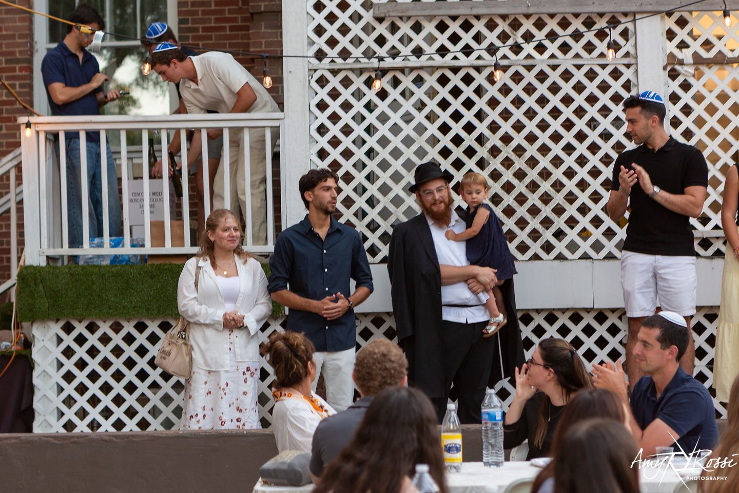 Nossen and Chaya speaking to a backyard full of students from the porch