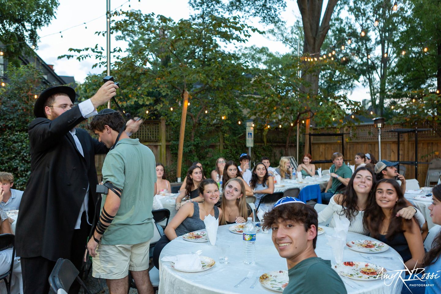 Rabbi Nossen raising a toast over a backyard full of students